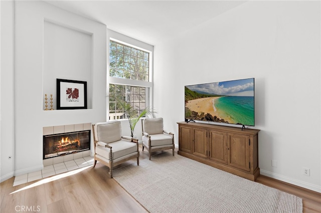 sitting room with a high ceiling, a fireplace, baseboards, and wood finished floors