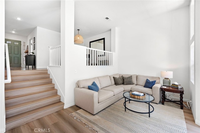 living area with wood finished floors, visible vents, baseboards, and stairs