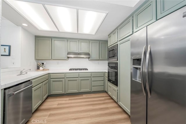 kitchen featuring light wood finished floors, tile countertops, stainless steel appliances, under cabinet range hood, and green cabinets