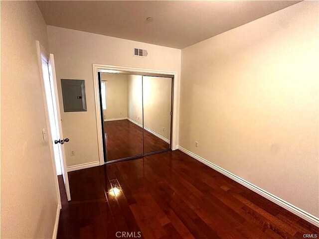 unfurnished bedroom featuring a closet, electric panel, and dark hardwood / wood-style floors