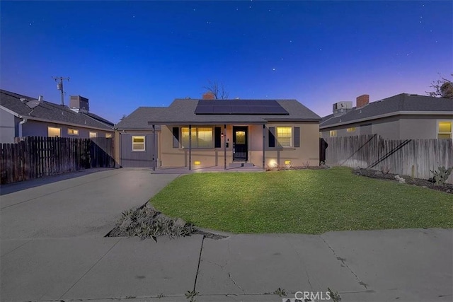 back house at dusk featuring central AC, a lawn, and solar panels