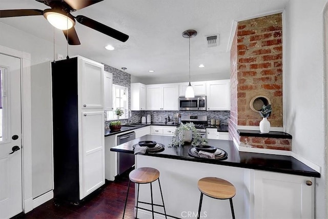 kitchen with a kitchen bar, appliances with stainless steel finishes, kitchen peninsula, pendant lighting, and white cabinets