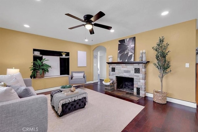 living room with a stone fireplace, wood-type flooring, and ceiling fan