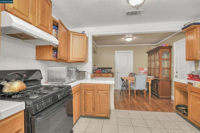 kitchen with tasteful backsplash, crown molding, gas stove, and light tile patterned floors