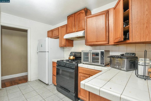 kitchen featuring black gas range oven, light tile patterned floors, white refrigerator, tile counters, and decorative backsplash