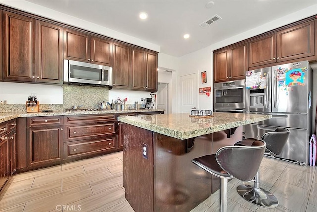 kitchen with a kitchen bar, tasteful backsplash, a center island, stainless steel appliances, and light stone countertops