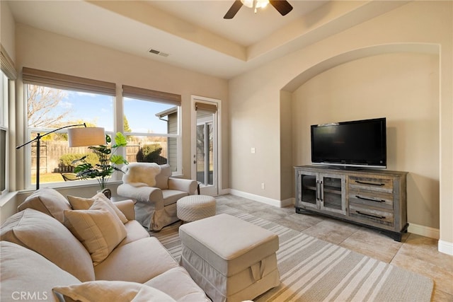 tiled living room with ceiling fan and a raised ceiling