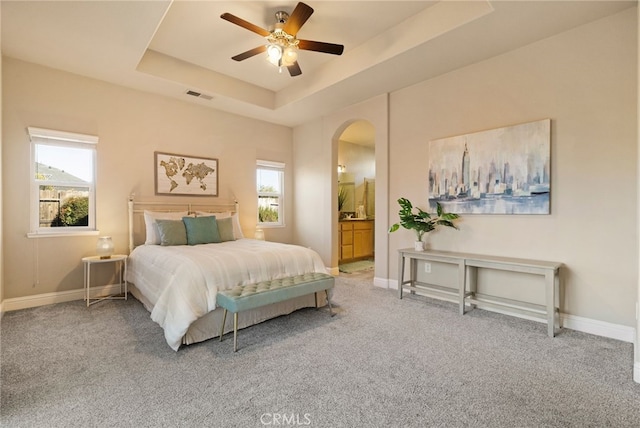 bedroom featuring carpet flooring, connected bathroom, a tray ceiling, and multiple windows