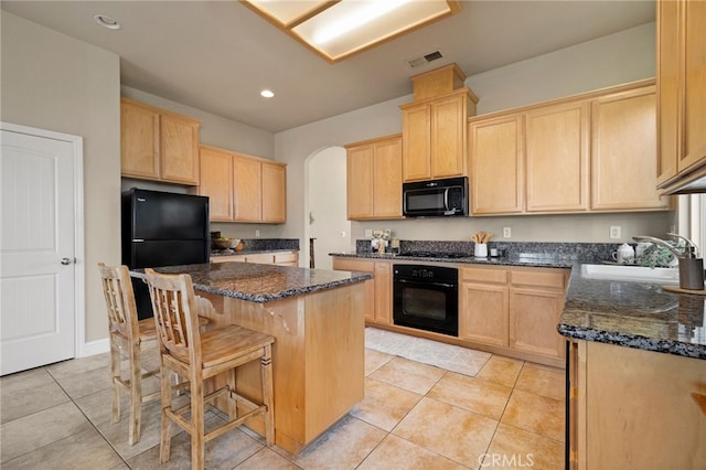 kitchen with sink, a center island, dark stone countertops, light brown cabinets, and black appliances