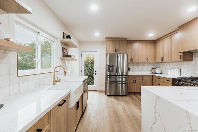 kitchen featuring appliances with stainless steel finishes, sink, light stone counters, and light wood-type flooring