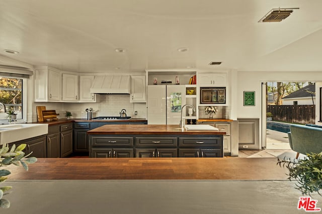 kitchen featuring white cabinetry, premium range hood, sink, and butcher block countertops