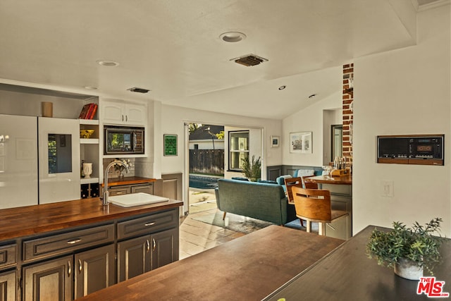 kitchen with wood counters, sink, white cabinetry, vaulted ceiling, and white refrigerator