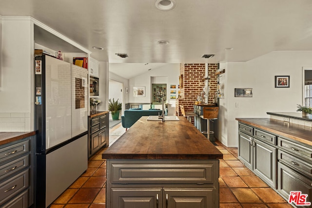 kitchen with a kitchen island, vaulted ceiling, fridge, and wooden counters