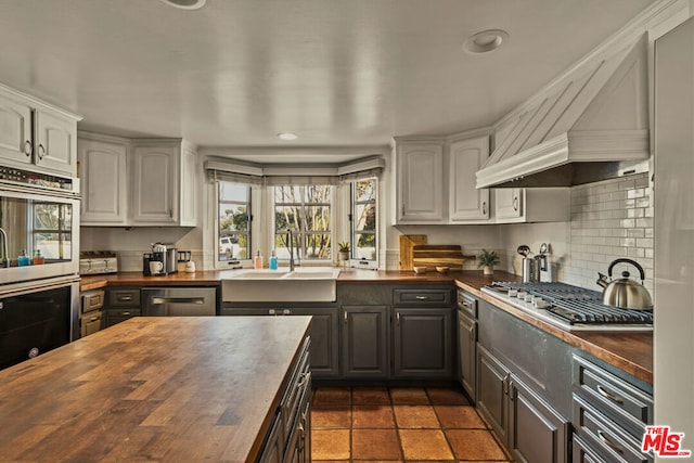 kitchen with stainless steel appliances, premium range hood, and butcher block countertops