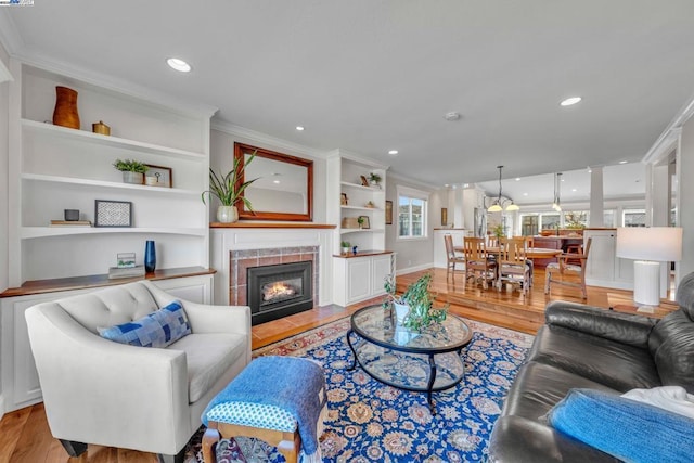 living room featuring built in features, ornamental molding, light hardwood / wood-style floors, and a tile fireplace