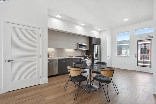 kitchen featuring lofted ceiling, light hardwood / wood-style flooring, gray cabinetry, backsplash, and stainless steel appliances