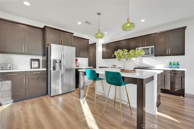 kitchen with light hardwood / wood-style flooring, hanging light fixtures, dark brown cabinets, stainless steel appliances, and an island with sink