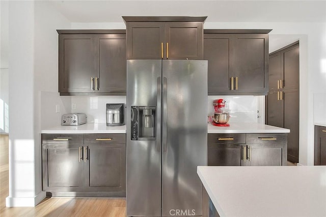 kitchen featuring dark brown cabinets, stainless steel fridge with ice dispenser, decorative backsplash, and light wood-type flooring