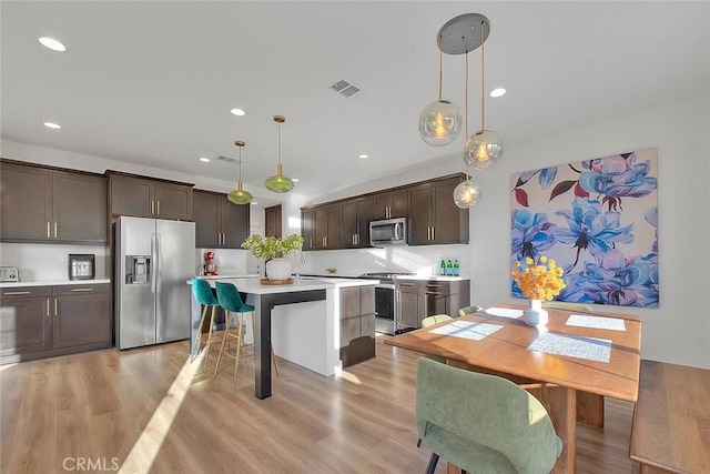 kitchen with appliances with stainless steel finishes, dark brown cabinets, light hardwood / wood-style floors, and decorative light fixtures