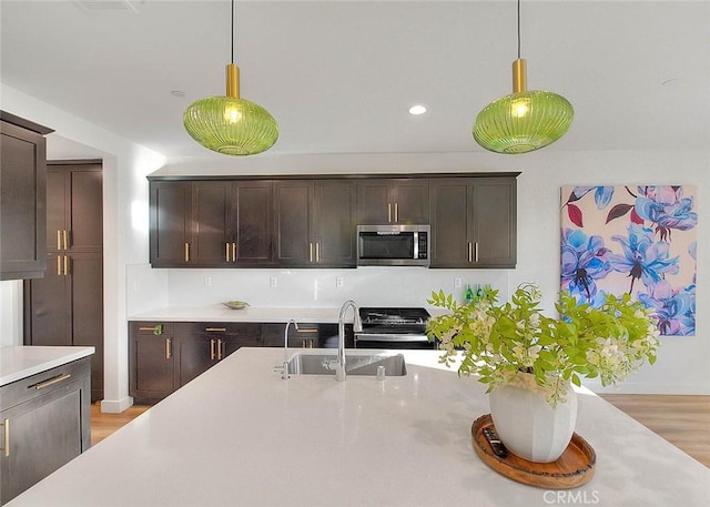 kitchen featuring sink, hanging light fixtures, dark brown cabinetry, stainless steel appliances, and light hardwood / wood-style flooring