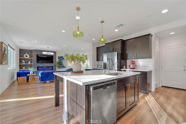 kitchen featuring sink, hanging light fixtures, a kitchen island with sink, stainless steel appliances, and dark brown cabinets