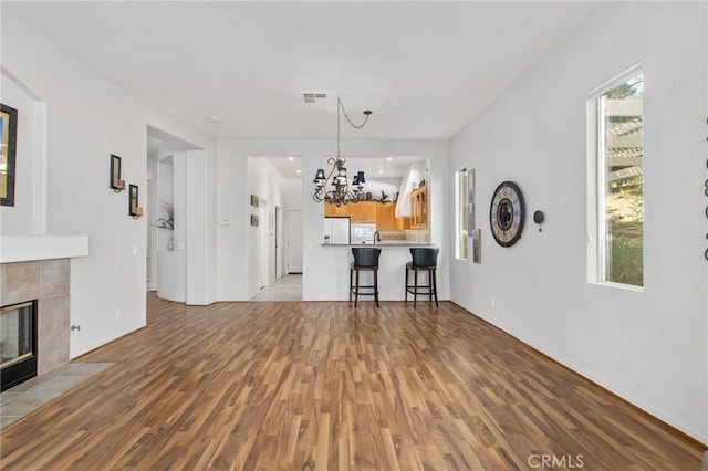 unfurnished living room with an inviting chandelier, a tiled fireplace, and light hardwood / wood-style floors