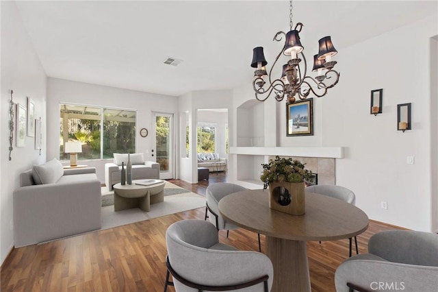 dining room featuring a tiled fireplace, hardwood / wood-style floors, and a notable chandelier