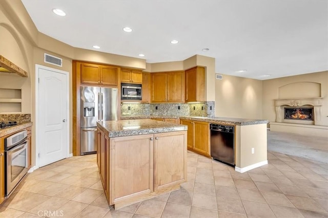 kitchen featuring appliances with stainless steel finishes, a fireplace, tasteful backsplash, a center island, and light stone countertops