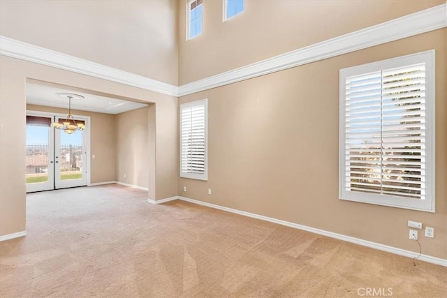 carpeted empty room featuring crown molding, french doors, a chandelier, and a high ceiling