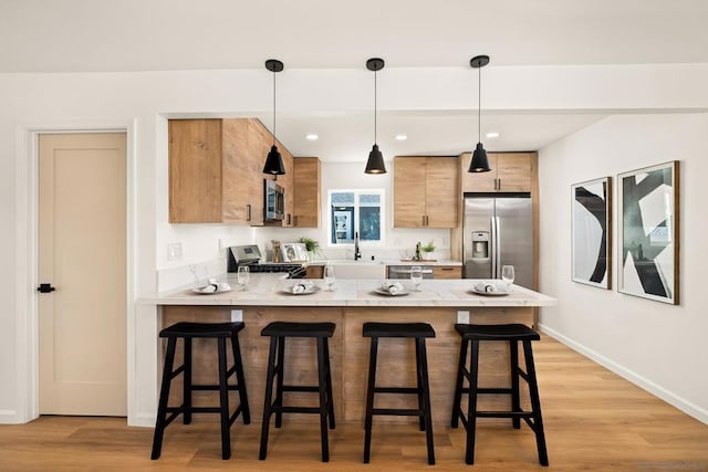 kitchen featuring appliances with stainless steel finishes, decorative light fixtures, a kitchen breakfast bar, kitchen peninsula, and light wood-type flooring