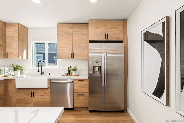 kitchen featuring stainless steel appliances, light stone countertops, sink, and light hardwood / wood-style floors