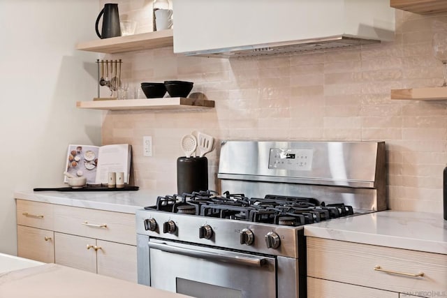 kitchen featuring light stone counters, backsplash, and stainless steel gas range