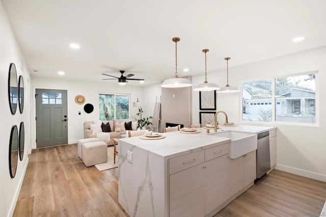 kitchen featuring sink, hanging light fixtures, light wood-type flooring, stainless steel dishwasher, and light stone countertops