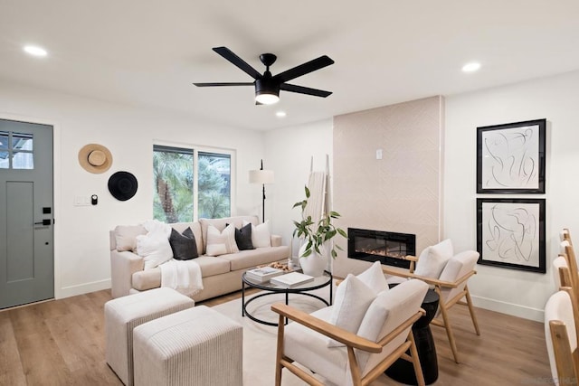 living room featuring ceiling fan, a tiled fireplace, and light hardwood / wood-style floors