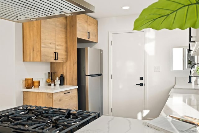 kitchen with gas stovetop, sink, stainless steel refrigerator, and range hood