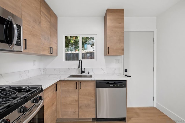 kitchen with appliances with stainless steel finishes, light brown cabinetry, sink, light hardwood / wood-style floors, and light stone countertops