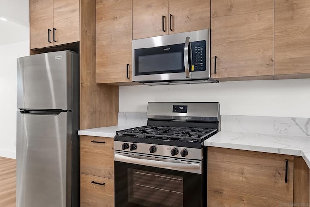 kitchen featuring stainless steel appliances, light stone countertops, and hardwood / wood-style floors