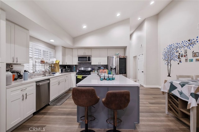 kitchen with appliances with stainless steel finishes, white cabinetry, hardwood / wood-style floors, a kitchen island, and decorative backsplash