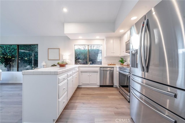 kitchen featuring tile countertops, white cabinetry, kitchen peninsula, stainless steel appliances, and light hardwood / wood-style flooring