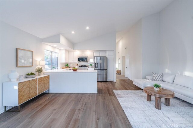 kitchen with appliances with stainless steel finishes, hardwood / wood-style floors, high vaulted ceiling, white cabinets, and kitchen peninsula