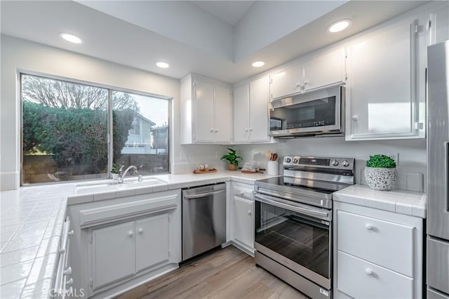 kitchen featuring sink, white cabinetry, tile countertops, stainless steel appliances, and light hardwood / wood-style floors