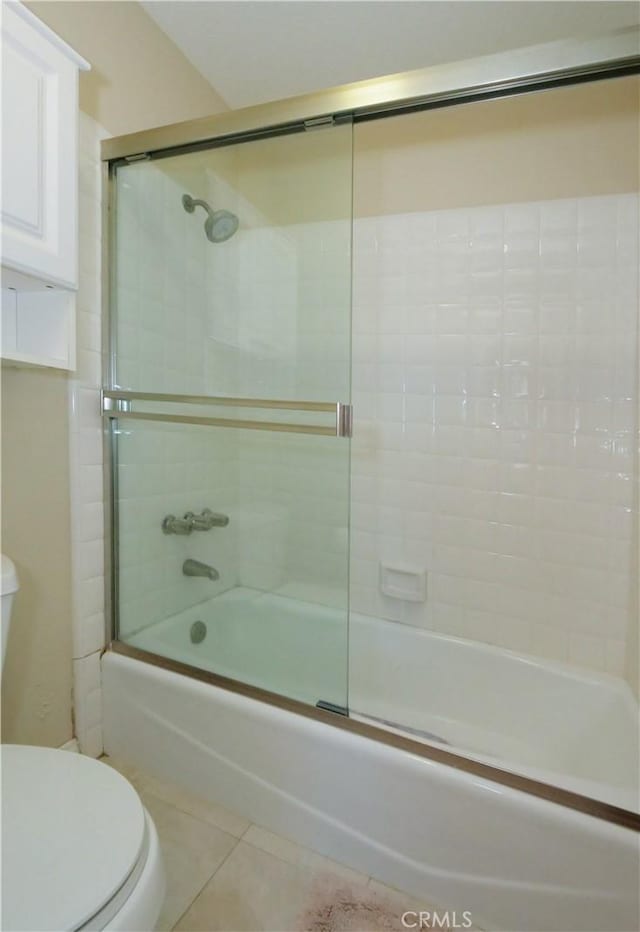 bathroom with combined bath / shower with glass door, tile patterned floors, and toilet