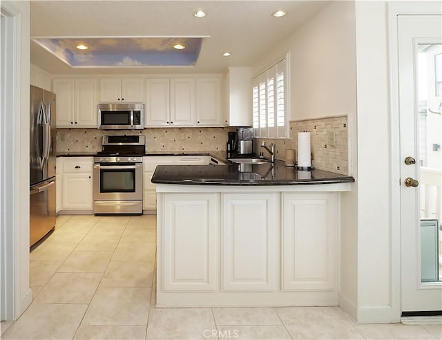 kitchen featuring sink, light tile patterned floors, appliances with stainless steel finishes, a tray ceiling, and kitchen peninsula