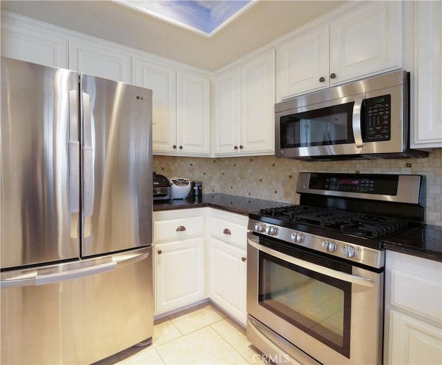 kitchen with appliances with stainless steel finishes, white cabinetry, backsplash, dark stone counters, and light tile patterned floors