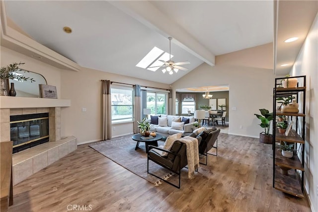 living room featuring ceiling fan, lofted ceiling with skylight, a tiled fireplace, and hardwood / wood-style floors