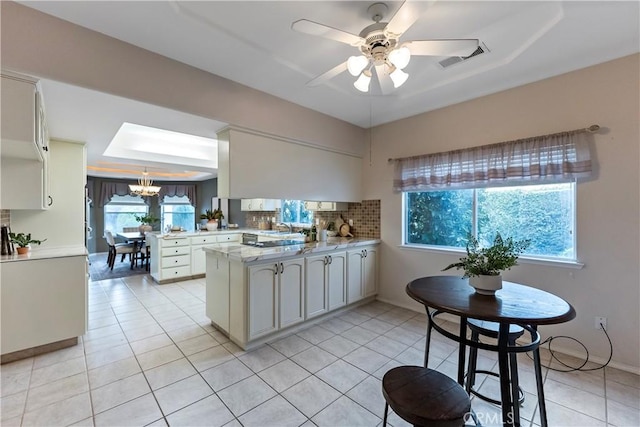 kitchen with white cabinetry, decorative light fixtures, kitchen peninsula, a raised ceiling, and decorative backsplash