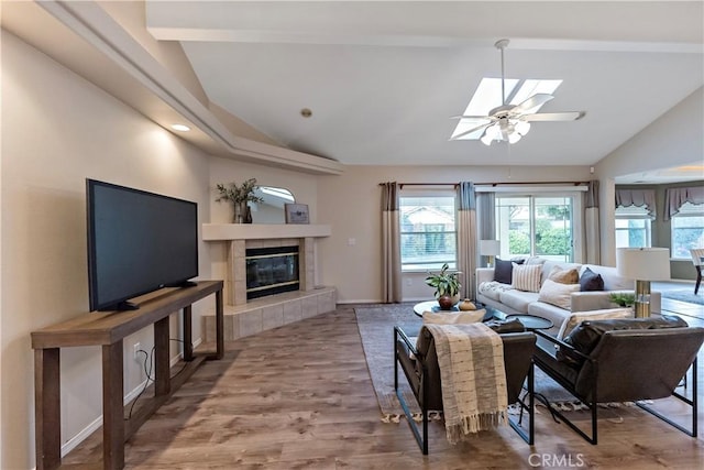 living room featuring ceiling fan, wood-type flooring, lofted ceiling with skylight, and a tiled fireplace