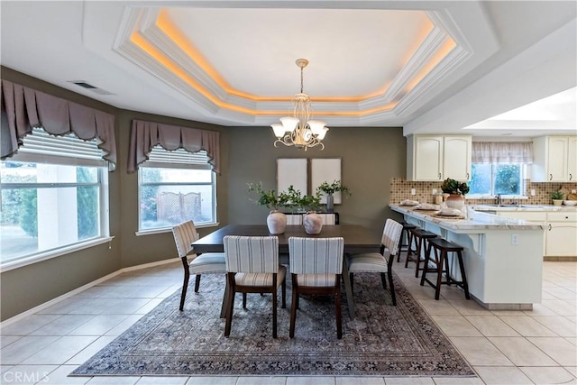 tiled dining space with a raised ceiling, crown molding, sink, and a notable chandelier