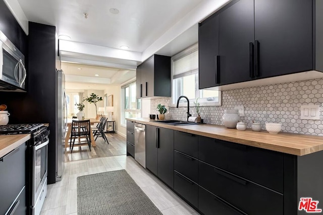 kitchen with appliances with stainless steel finishes, wood counters, sink, decorative backsplash, and a tray ceiling