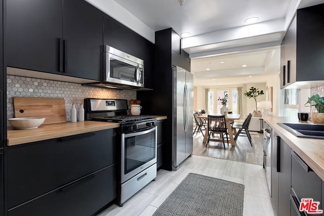 kitchen with tasteful backsplash, wooden counters, a raised ceiling, and appliances with stainless steel finishes